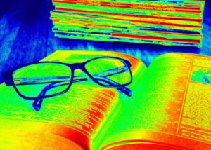 Image of open book with glasses on top. Image has a filter with green, yellow, and red.