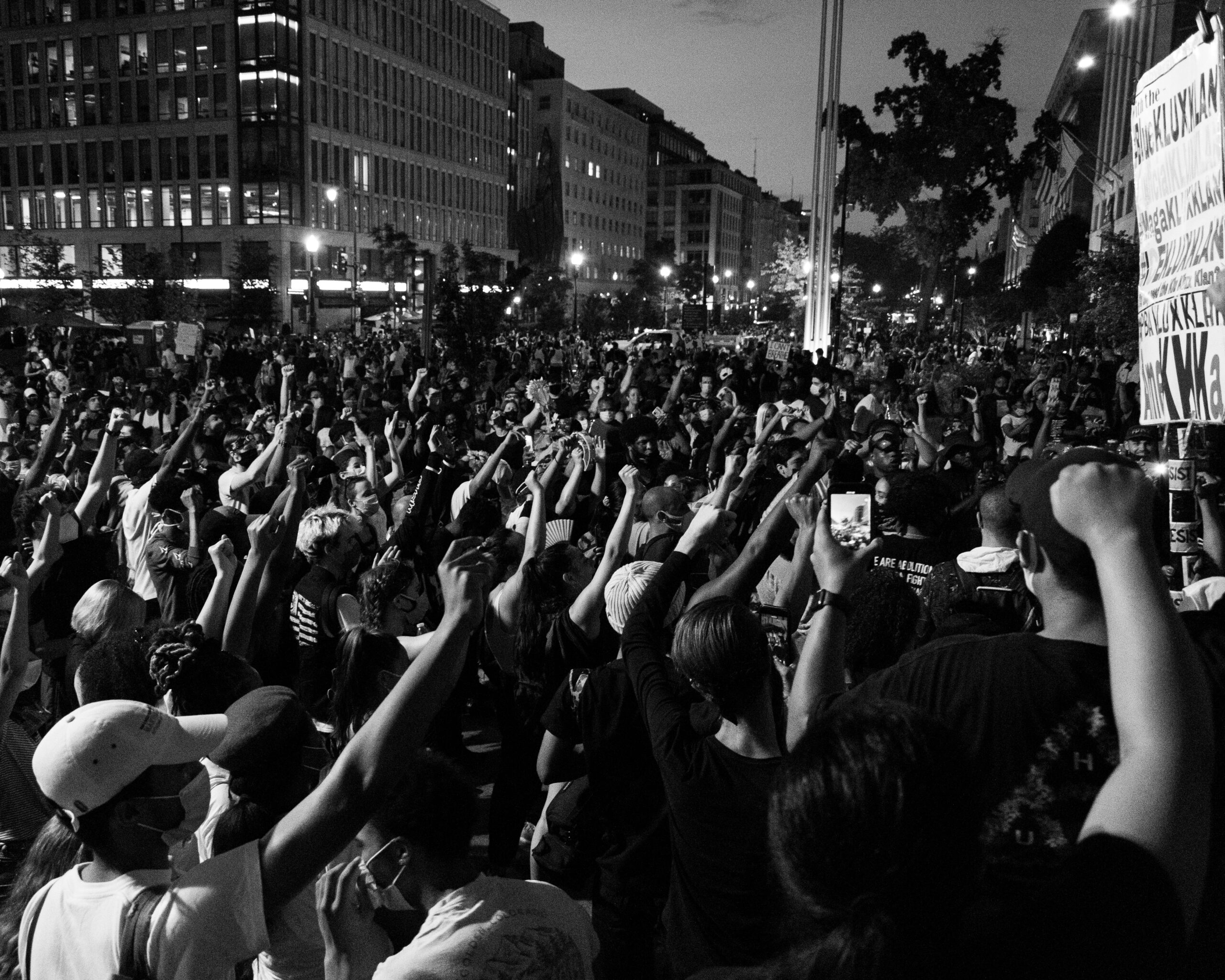 Black and white street scene of protest with people with fists raised.